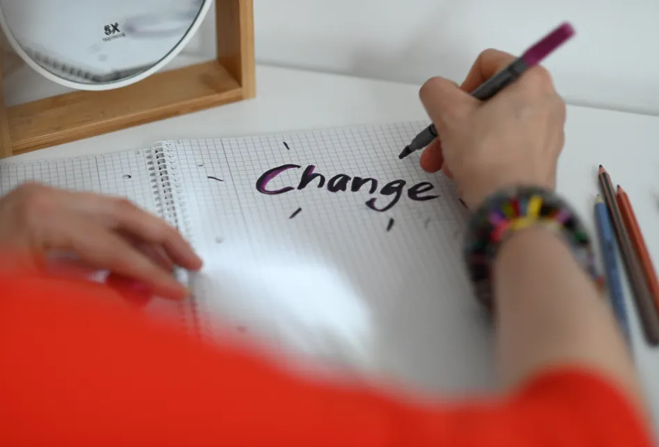 Eine Hand schreibt 'Change' auf einen Collegeblock